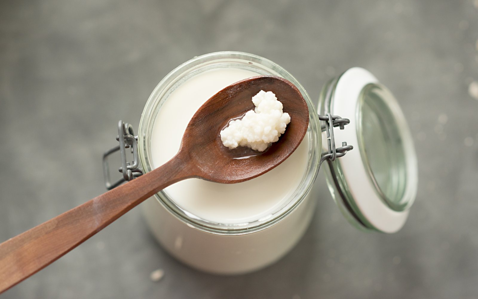 Grains de kéfir de lait sur une cuillère en bois au-dessus d'un bocal