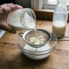 Kéfir de lait maison versé à travers une passoire pour récupérer les grains